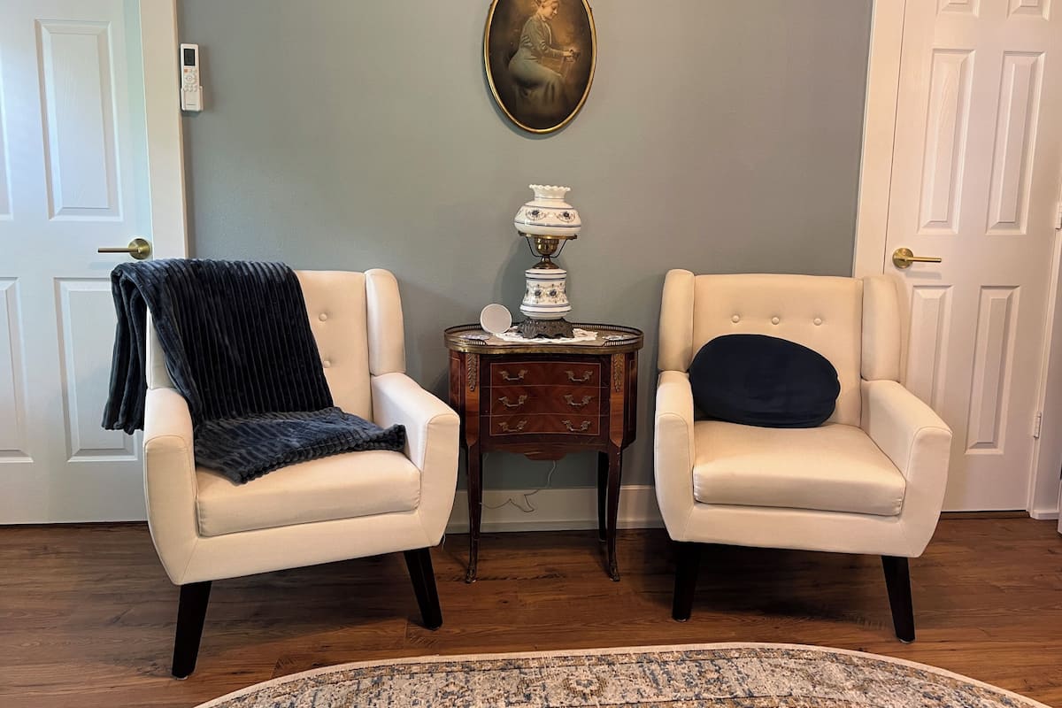 Two armchairs with a small table between them, a decorative lamp, and a framed picture on the wall.
