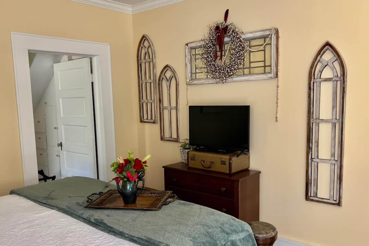 A bedroom with a bed, a dresser, a television on a suitcase, and decorative window frames.