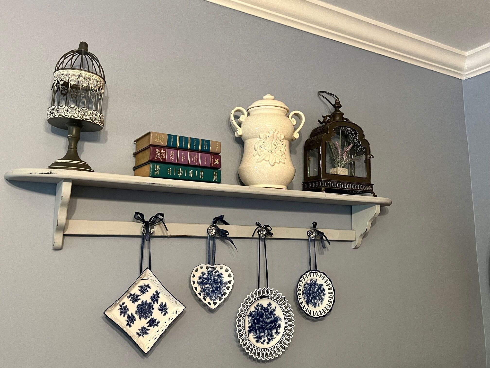 Una estantería con objetos decorativos como una jaula de pájaros, libros, un florero y adornos colgantes.