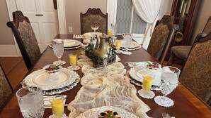 A dining table set with ornate white plates, clear glassware, and a decorative centerpiece.