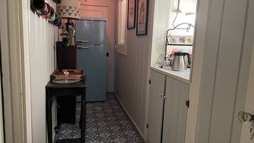 A narrow hallway with a blue refrigerator, a coffee shop sign, and a table with a vase.