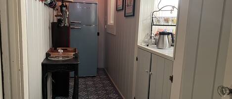 Un pasillo estrecho con un refrigerador azul, un letrero de cafetería y una mesa con un jarrón.