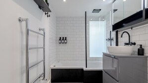 A modern bathroom with a bathtub, a sink, and a glass shower enclosure. - Luxurious & Chic 2BD Warehouse Flat - Old Street! (London)