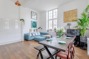 Una sala de estar moderna con un sofá seccional azul, una mesa de comedor con sillas y un piano.