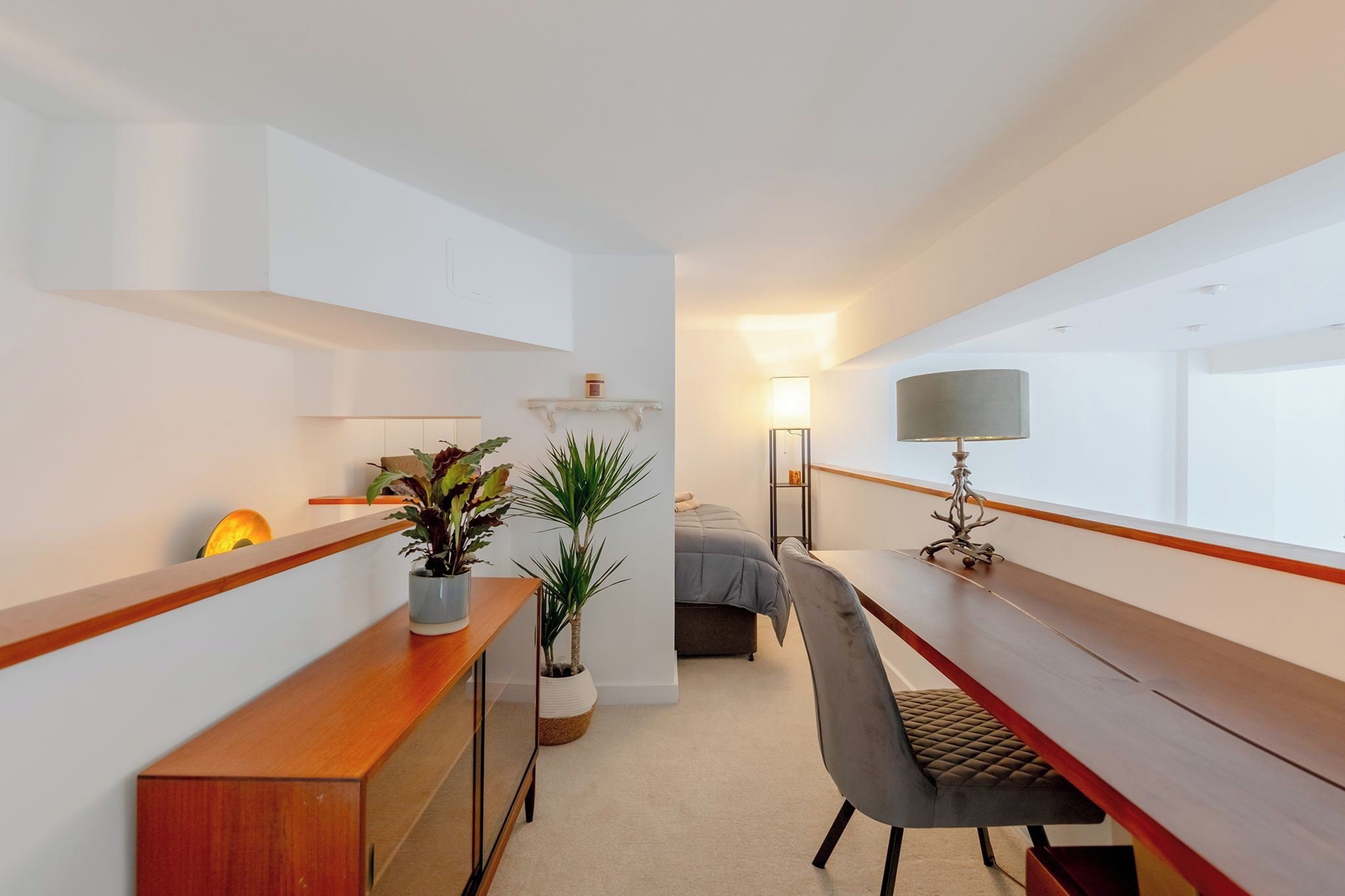 A modern, well-lit room with a wooden desk, a chair, a bed, and a bedside table.