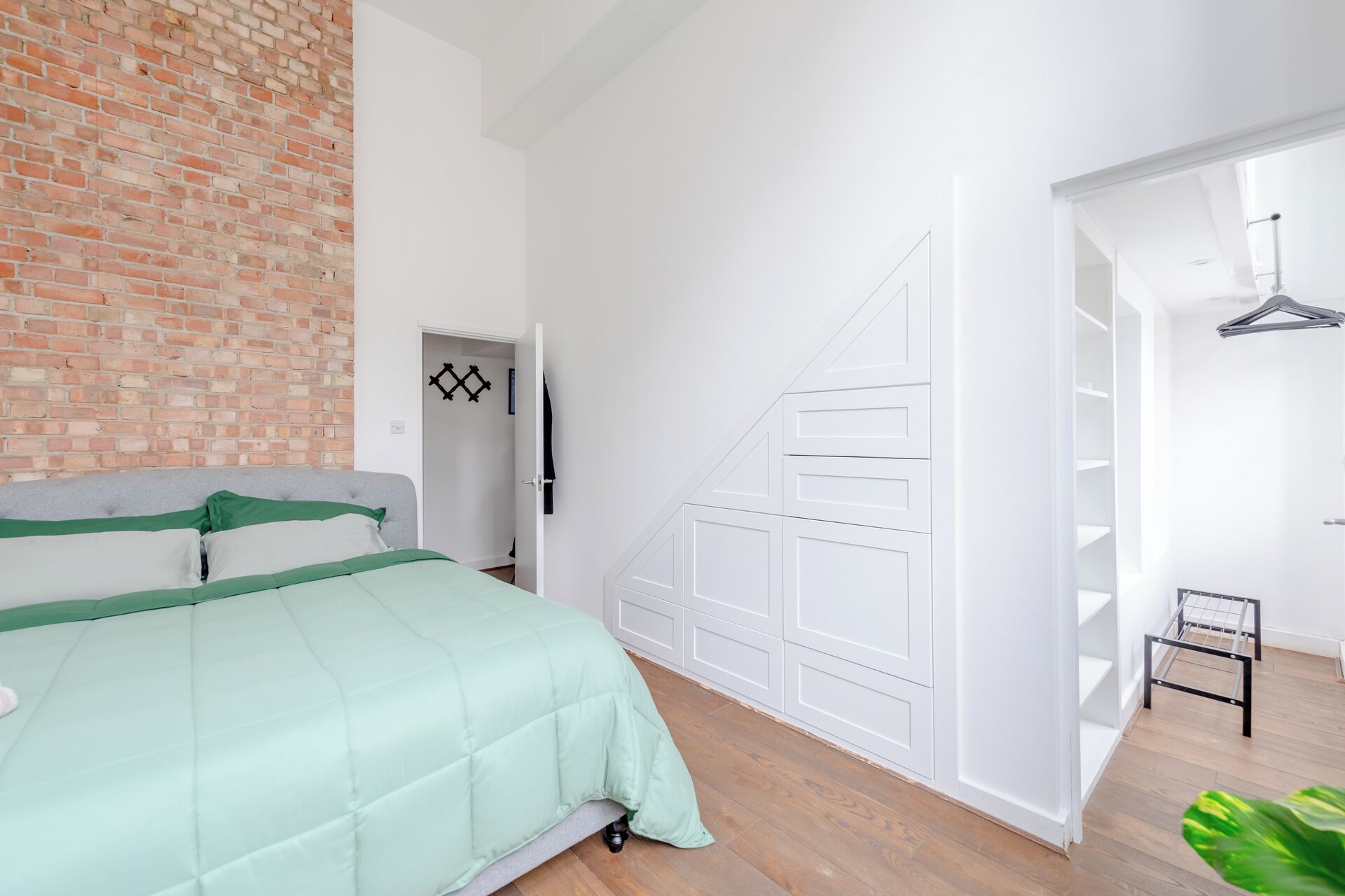 A bedroom with a brick wall, a bed with green bedding, a white wardrobe, and a white door with a geometric design.