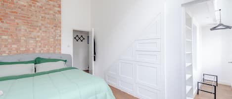 Un dormitorio con pared de ladrillo, cama con ropa de cama verde, armario blanco y puerta blanca con diseño geométrico.