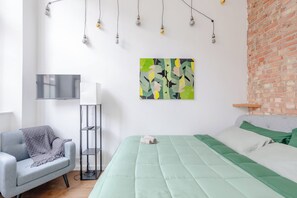 Quarto moderno com cama, poltrona, televisão e um quadro.