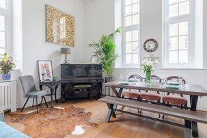 Comedor con mesa de madera dispuesta para cuatro personas, un piano negro, una planta grande y una alfombra de cuero de vaca.