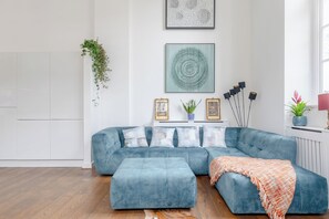 Un salon moderne avec un canapé d’angle bleu, un plaid à motifs et une plante en pot.