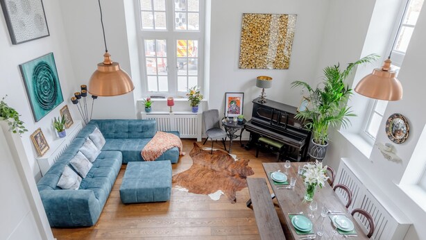 A spacious living room with a blue sofa, a dining table set for four, a piano, and a cowhide rug. - Luxurious & Chic 2BD Warehouse Flat - Old Street! (London)