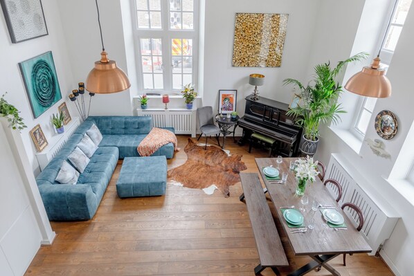 A spacious living room with a blue sofa, a dining table set for four, a piano, and a cowhide rug.