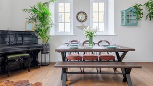 A dining area with a wooden table set for four, surrounded by chairs, a bench, and a piano. - Luxurious & Chic 2BD Warehouse Flat - Old Street! (London)
