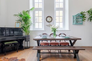 Un comedor con mesa de madera dispuesta para cuatro personas, rodeada de sillas, un banco y un piano.