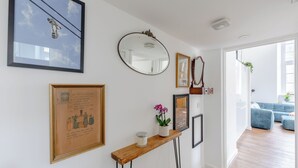 A hallway with framed artwork, a mirror, and a small table with a candle and orchid. - Luxurious & Chic 2BD Warehouse Flat - Old Street! (London)