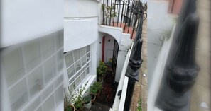 A narrow alleyway with a white building on one side and a black metal fence on the other. There are potted plants along the alley. - Modern 1-Bed APT | Heart of Brighton & Sea Views (Brighton and Hove)