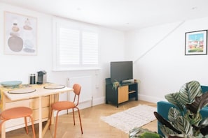 A modern living room with a dining area, a flat-screen TV, and a large plant.