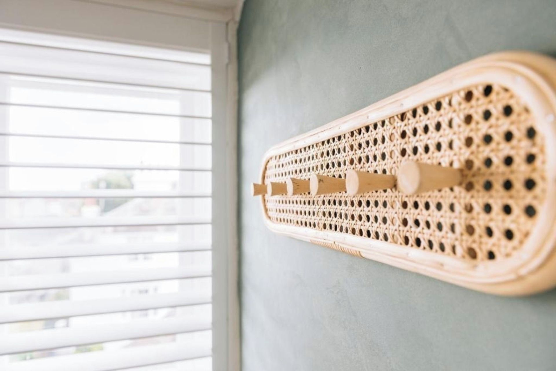 A wall-mounted wooden rack with a woven pattern, likely for storage, against a grey wall with a window in the background.