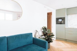 A modern living room with a blue sofa, a round mirror, a potted plant, and a kitchen area with a refrigerator and oven. - Modern 1-Bed APT | Heart of Brighton & Sea Views (Brighton and Hove)