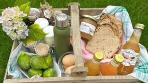 A wooden tray with food items including bread, eggs, and jars of preserves, placed on grass.