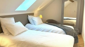 A bedroom with a sloped ceiling, a skylight, a large mirror, and a bed with white bedding.