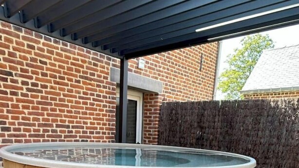 A wooden hot tub with a glass top, surrounded by a brick wall and a wooden fence.