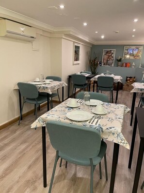 A dining area with tables set for four, chairs, and a ceiling-mounted air conditioning unit.