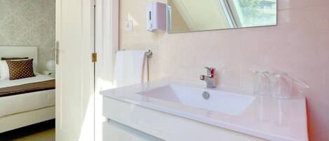 A modern bathroom with a white sink, a large mirror, and a window above the sink.