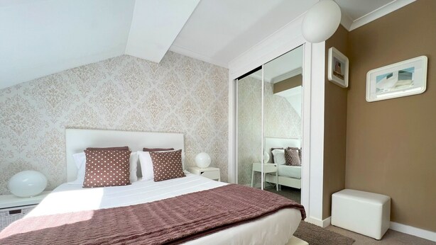 A modern bedroom with a large bed, a bedside table, a nightstand, a mirror, and a small white cabinet. - O'Porto Seven - Guest House (Porto)