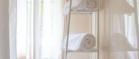 A bathroom with a bathtub, a towel rack with towels, and sheer curtains.