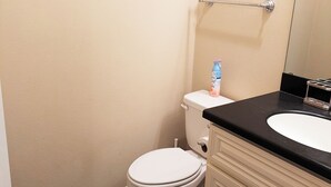 A bathroom with a toilet, a sink, a mirror, and a clock on the wall.