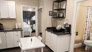 A compact hotel room with a kitchenette, a dining area, and a shower.