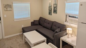 A living room with a sectional sofa, a small white table, a lamp, and a ceiling fan.