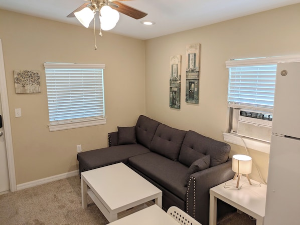 A living room with a sectional sofa, a small white table, a lamp, and a ceiling fan.