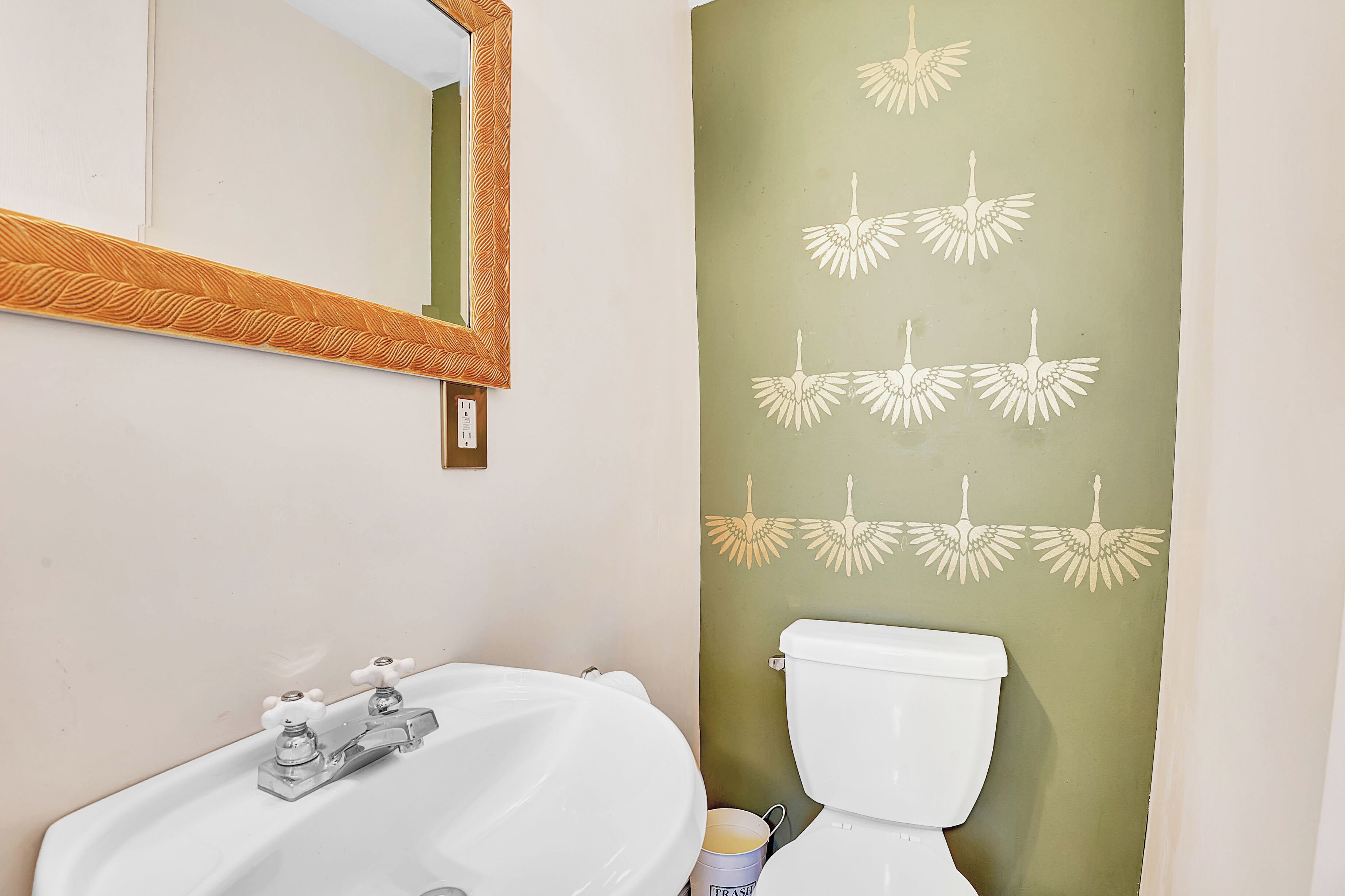 A bathroom with a white sink, a mirror with a wooden frame, and a toilet with a green wall.