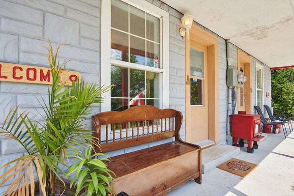 A wooden bench outside a building with a 'WELCOME' sign, a red heater, and a door with a window. - 17463 County Rd 18 (South Stormont)