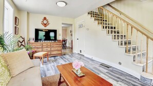 Ein Wohnzimmer mit Sofa, Couchtisch, Fernseher, Treppe und Essbereich.