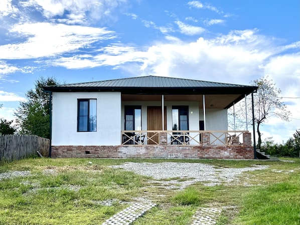 A single-story house with a covered porch, a brick foundation, and a gravel driveway.