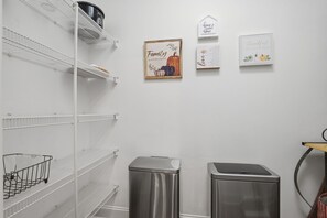 Un interior limpio y blanco con estanterías metálicas, un cubo de basura y detalles decorativos en la pared.