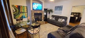 A living room with a fireplace, a sofa, a TV, and a dining area with a glass table and chairs.