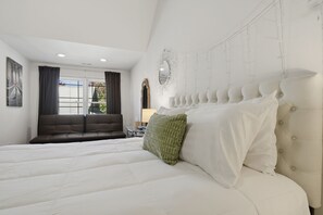 Un dormitorio con una cama grande, un sofá, un espejo y una ventana con cortinas.