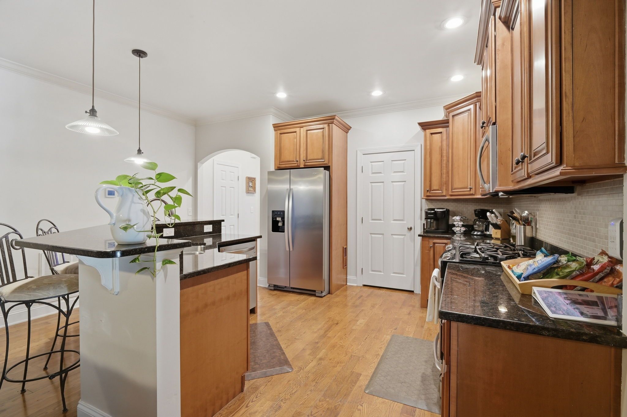 A modern kitchen with wooden cabinets, a stainless steel refrigerator, and a bar area with stools.