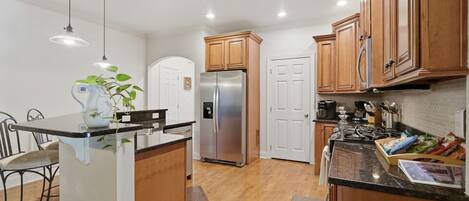 A modern kitchen with wooden cabinets, a stainless steel refrigerator, and a bar area with stools.