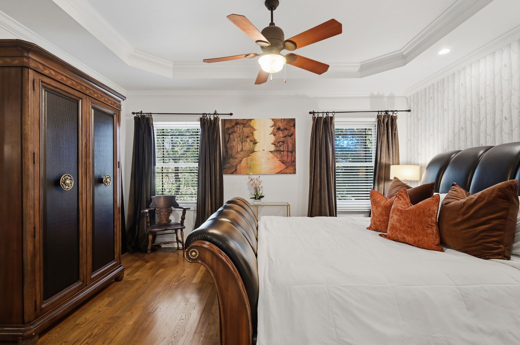 A bedroom with a large bed, a ceiling fan, a desk with a chair, and a large wardrobe.
