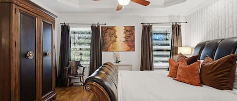 A bedroom with a large bed, a ceiling fan, a desk with a chair, and a large wardrobe.