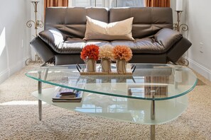 Una sala de estar con una mesa de centro de vidrio, un sofá de cuero y jarrones decorativos con flores.