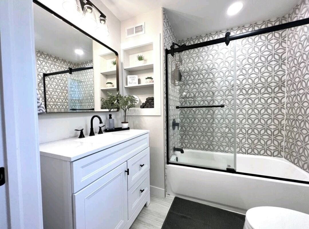 A modern bathroom with a white vanity, a large mirror, a shower with a geometric-patterned glass door, and a white bathtub.