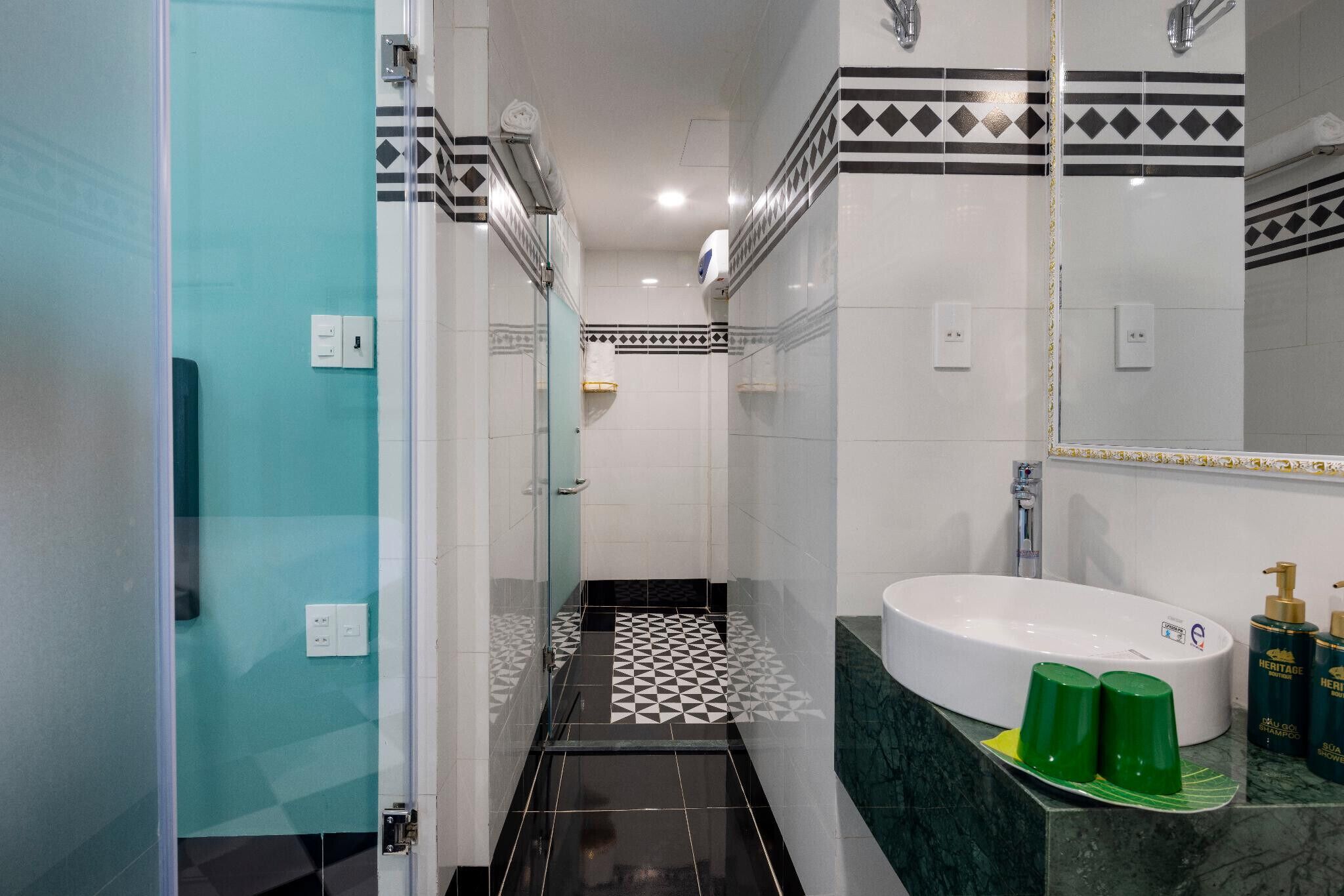 A modern bathroom with a glass shower enclosure, a white sink with a green soap dish, and a mirror with a decorative border.