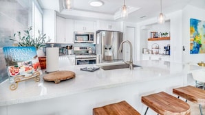 Una cocina moderna con armarios blancos, electrodomésticos de acero inoxidable y una isla central con taburetes.