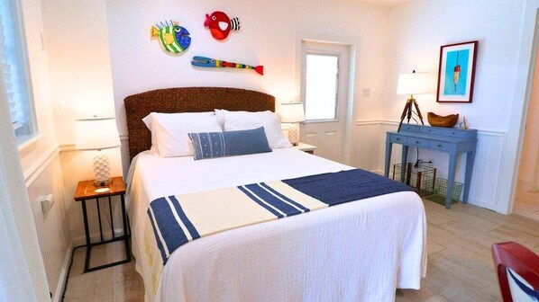 Un dormitorio con una cama grande, una mesita de noche, un escritorio y decoraciones en la pared, incluyendo figuras de peces.